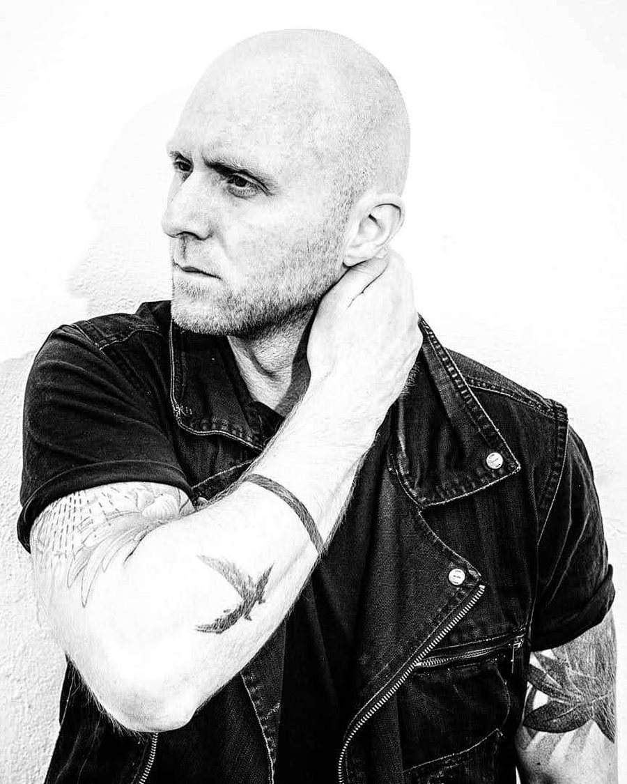 Ísak Morris in a black denim vest, hand resting on his neck, black-and-white portrait