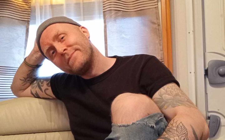 Ísak Morris in a black T-shirt and beanie, leaning back on a sofa